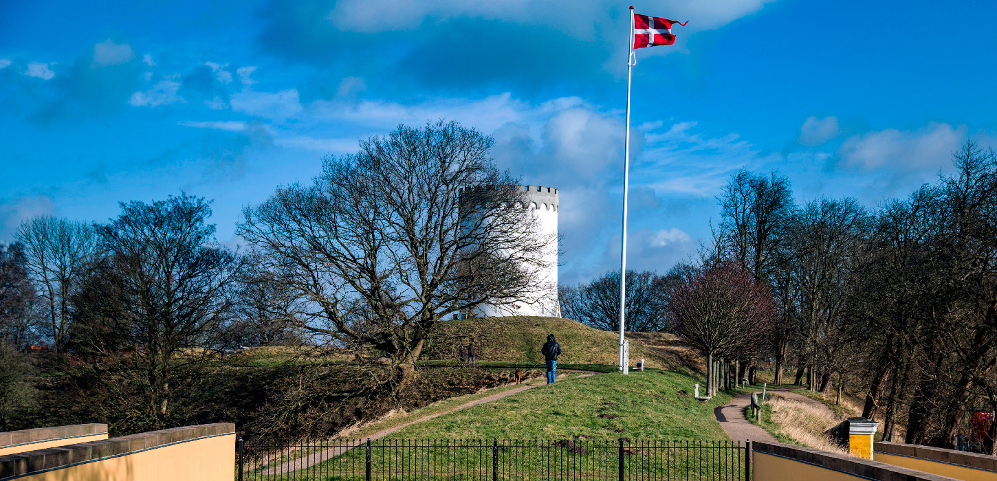 Par på gåtur langs Fredericia Vold i solskin – historisk voldanlæg omgivet af grønne omgivelser.