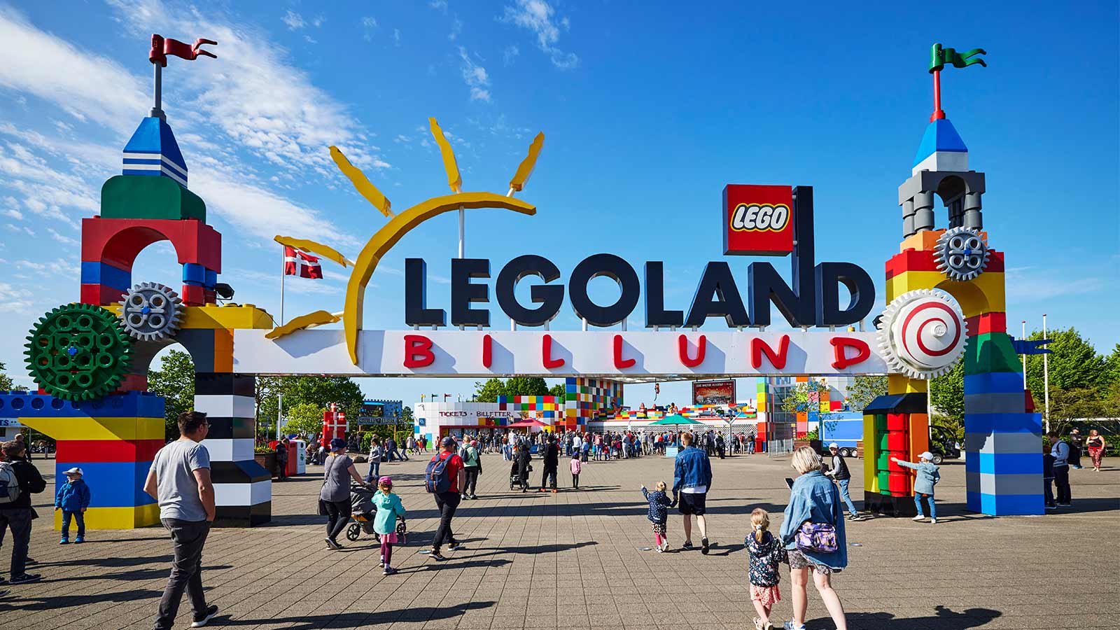 Das Eingangstor zum LEGOLAND mit den zwei Türmen aus LEGO® Steinen. Zahlreiche Gäste strömen in den Park, um diesen an einem Sommertag unter blauem Himmel zu genießen.
