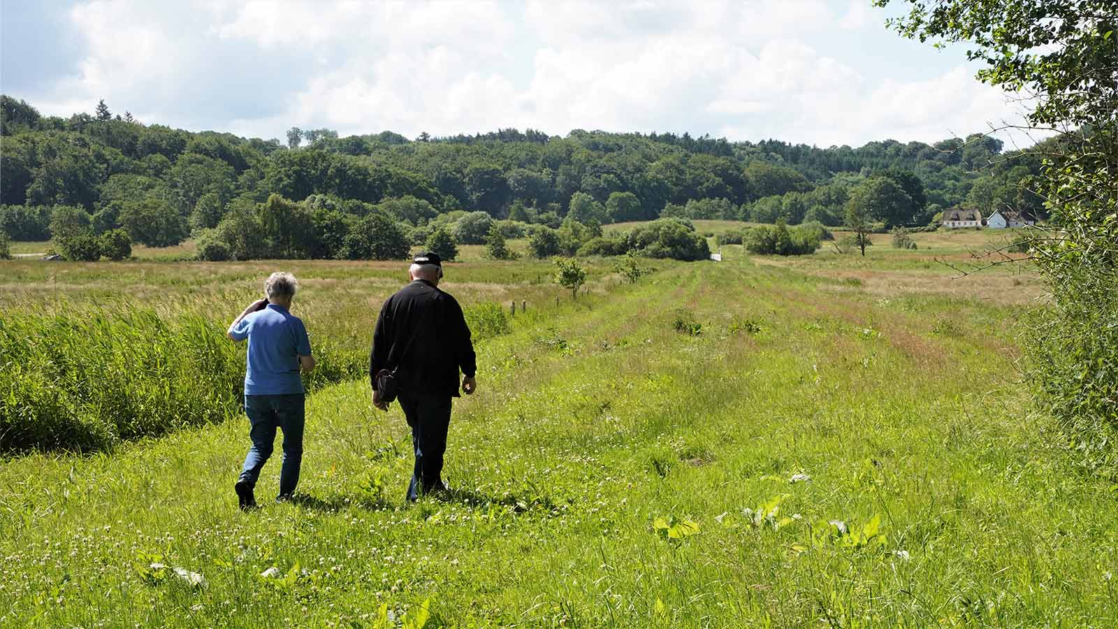 Two adults are walking in the sunshine on the green Ådal path at Ravningeboen.
