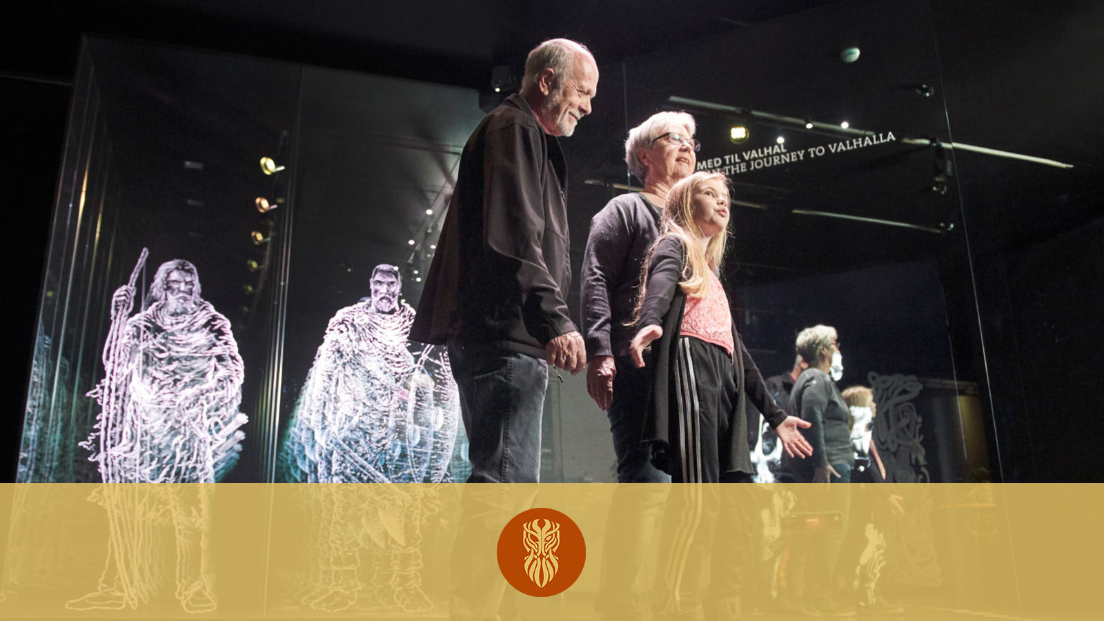 Several older and younger museum visitors form a chain in the interactive exhibition Journey to Valhalla. In the background are glowing Vikings.