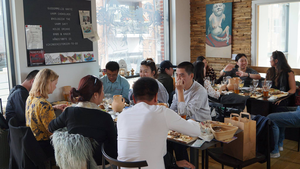 En gruppe mennesker hygger sig med at spise på Cafe SEJD, der ligger lige ved Kongernes Jelling