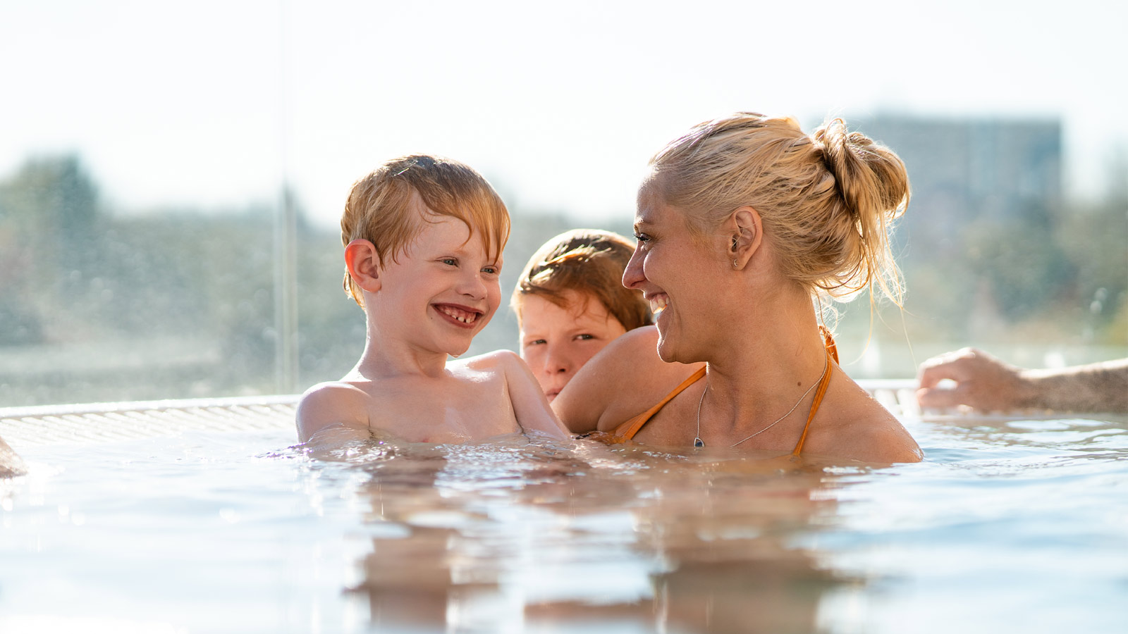 Mor og sønner nyder det udendørs spabad i Fredericia Idrætscenter. Der er udsigt udover hele Madsbyparken.
