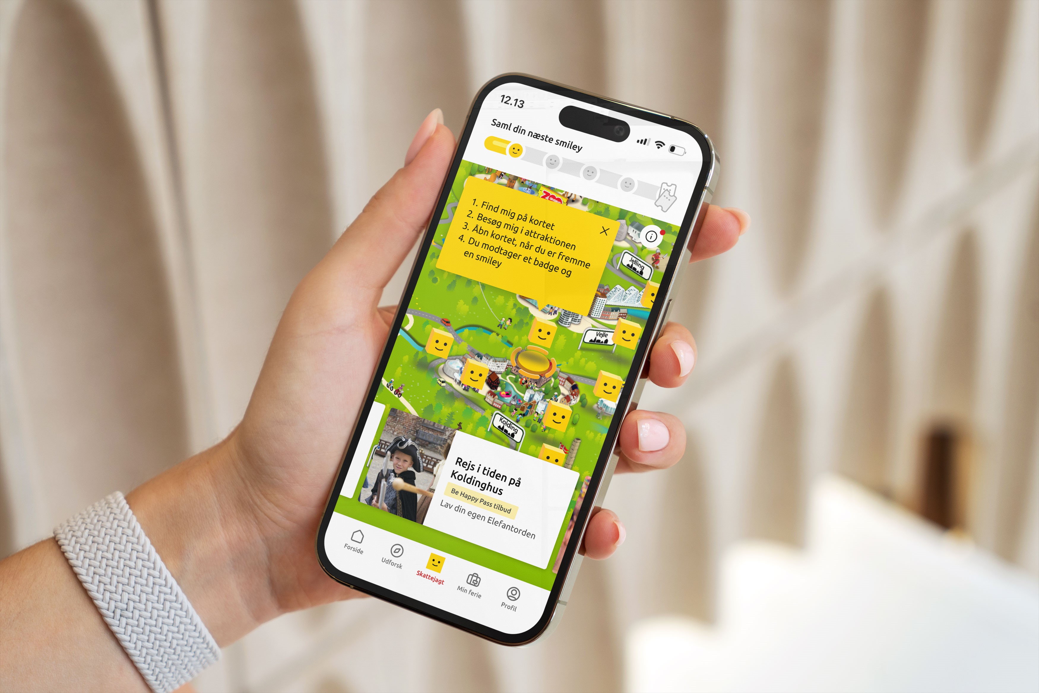 En hånd der holder en mobiltelefon, som viser LEGOLAND Billund Resort resortmap med skattejagten