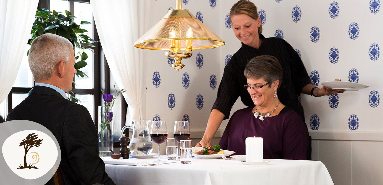 Gæster nyder middag på Filskov Kro, hvor en tjener serverer ved bordet. Kroen er en del af Small Wonders-ruten.
