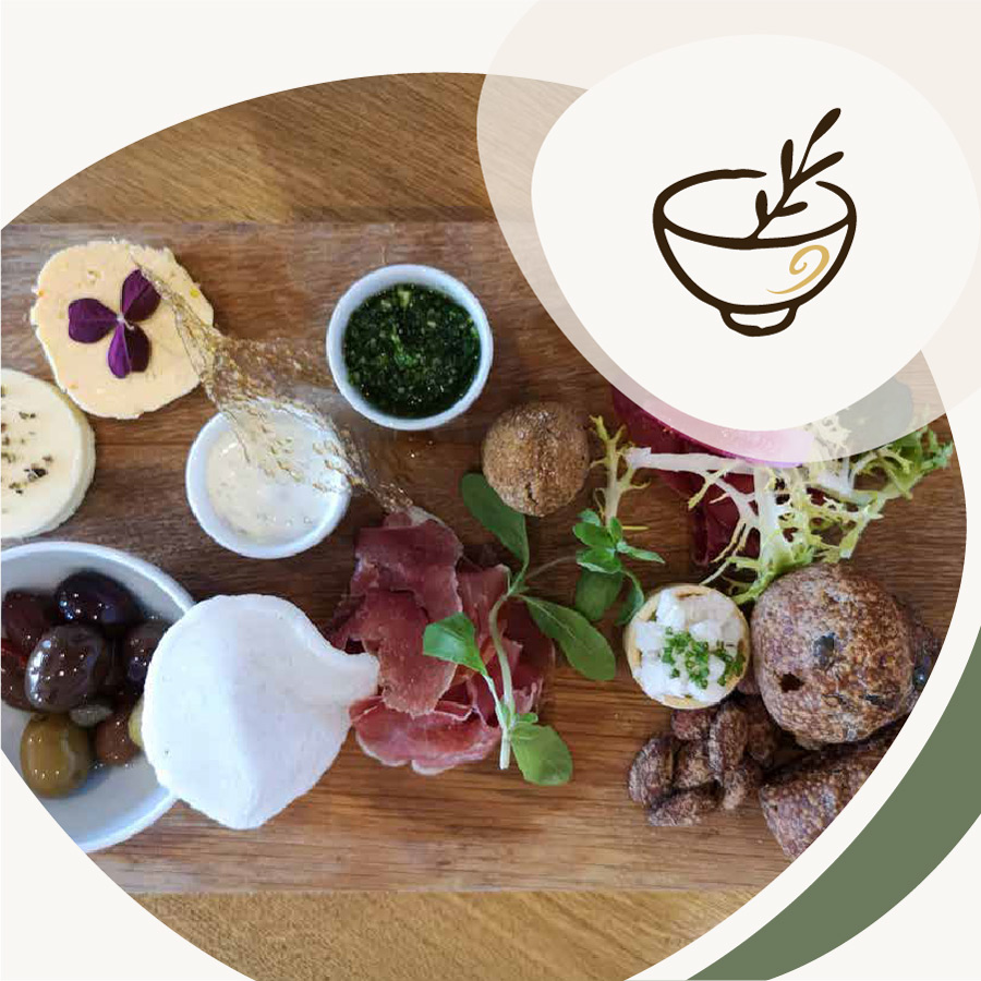 Anrettet tapasbræt med ost, kød, oliven, brød, grønt og små dip, illustreret med et ikon af en skål øverst til højre.