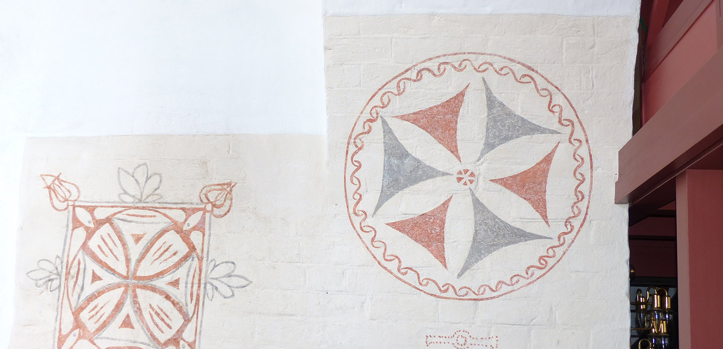To kalkmalerier på væggen i Vorbasse Kirke, med geometriske mønstre i røde og grå nuancer. Kirken er et stop på Kunstruten i Small Wonders – Heart of Jutland.