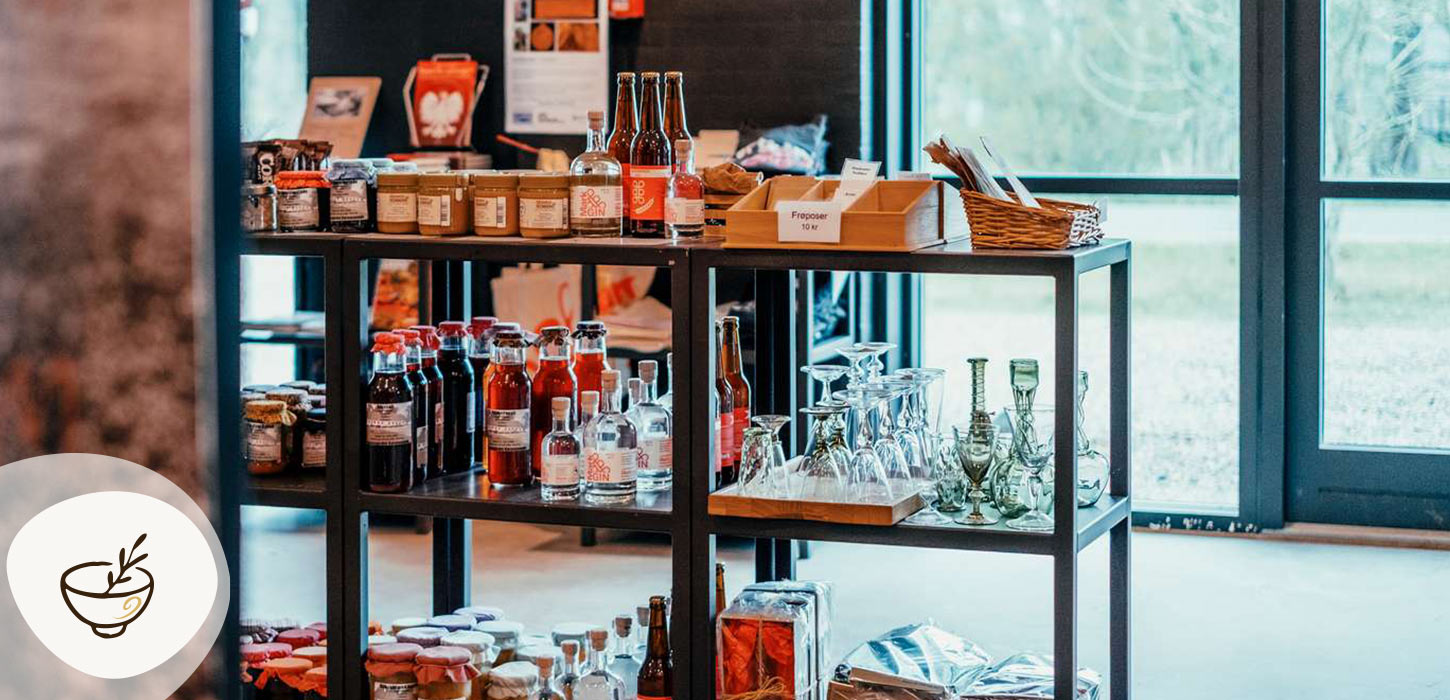 Butik på Museumsgården Karensminde med lokale fødevarer, flasker og glas på hylder, en del af Gastroruten i Small Wonders.