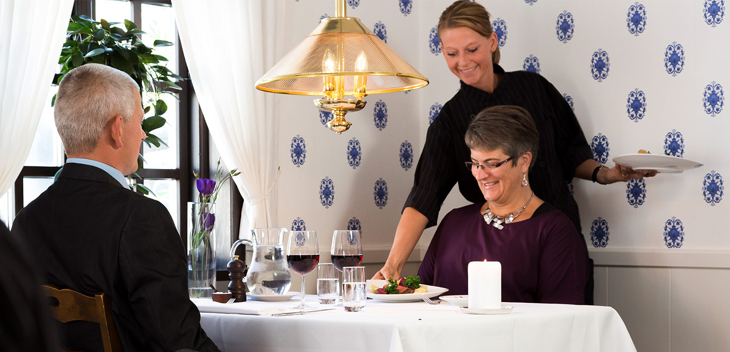 Gæster nyder middag på Filskov Kro, hvor en tjener serverer ved bordet. Kroen er en del af Gastroruten-ruten.