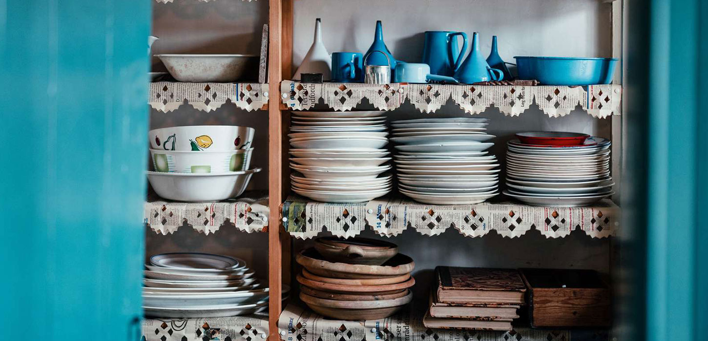 Interiør fra køkkenet på Museumsgården Karenminden. Der står tallerkener, skåle og kander på åbne hylder.