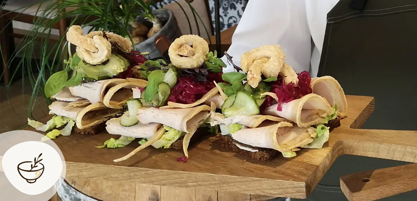 Smørrebrød fra Sdr. Omme Kro anrettet på træbræt med kød, friske grøntsager, sprøde toppings og urter. Kroen er en del af Gastroruten i Small Wonders.