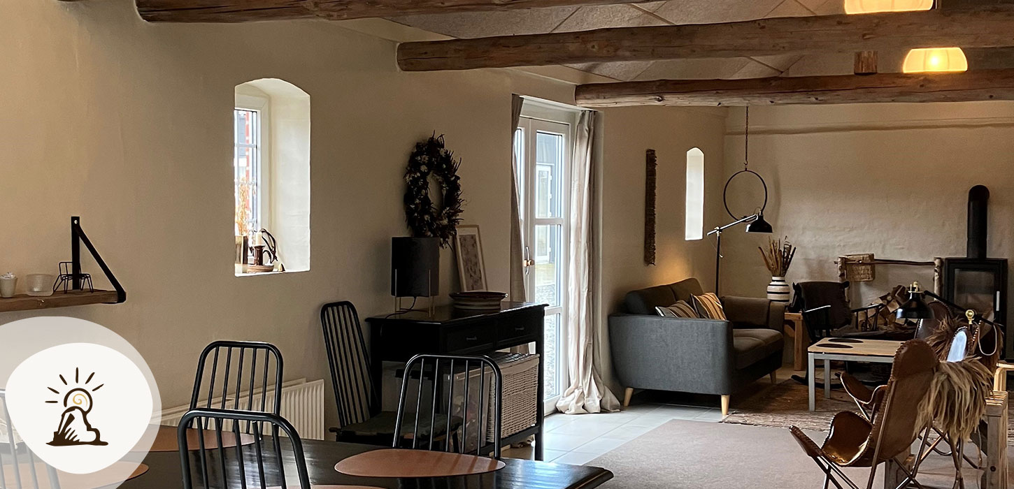 Lyst og hyggeligt loungeområde hos Bolding Apartments med sofaer, spiseplads og træbjælker. Et af overnatningsstederne på Kunstruten i Small Wonders – Heart of Jutland.