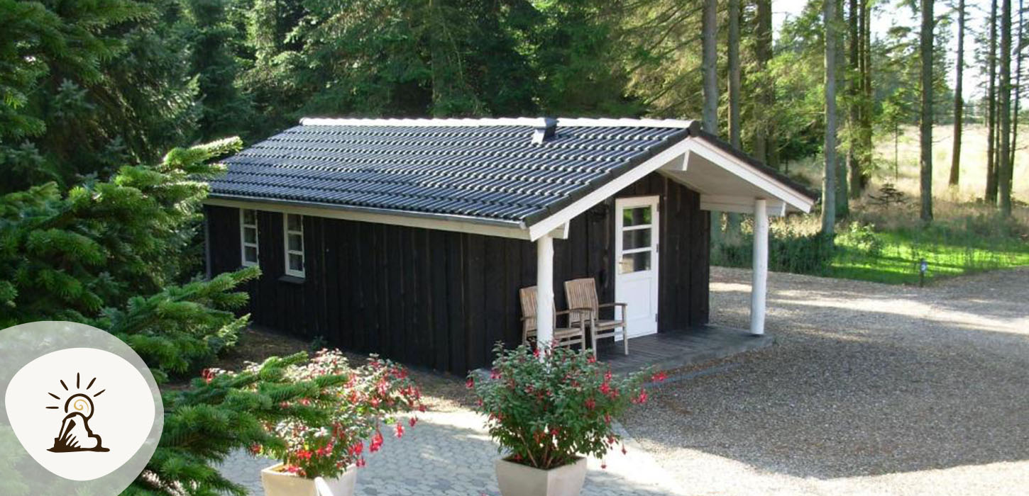 Lille sort træhytte med terrasse og natur omkring hos Gregersminde, et af overnatningsstederne på Kunstruten i Small Wonders – Heart of Jutland.