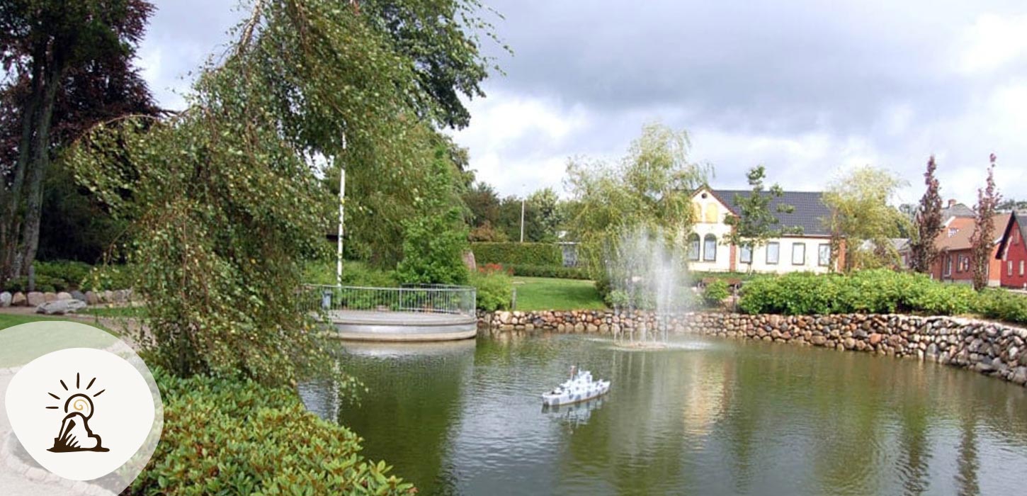 Vorbasse bypark med sø, vandfontæne og små huse i baggrunden. Vorbasse er en del af Kunstruten i Small Wonders – Heart of Jutland.