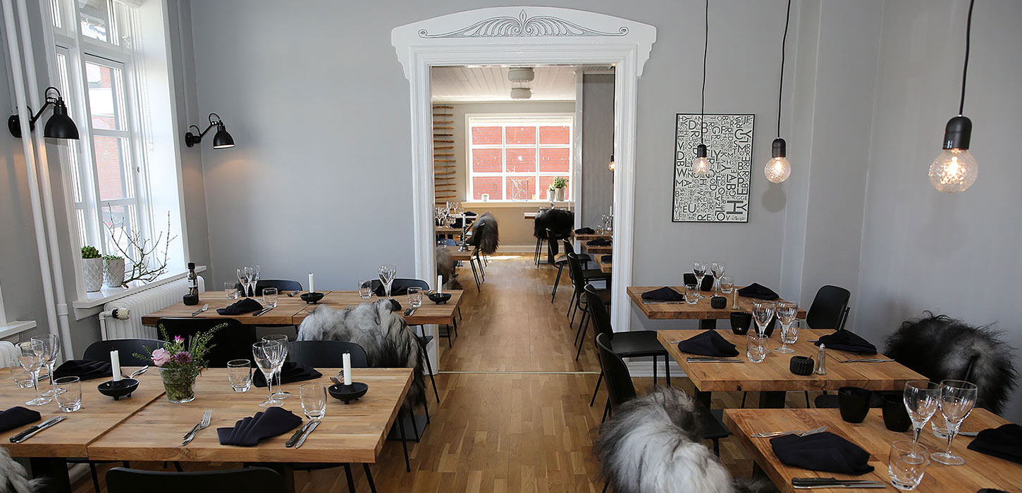 Lyst og moderne restaurantmiljø hos Spiseriet i Billund med dækkede træborde, sorte stole og hyggelige detaljer. En del af spiseoplevelserne på Small Wonders-ruterne.