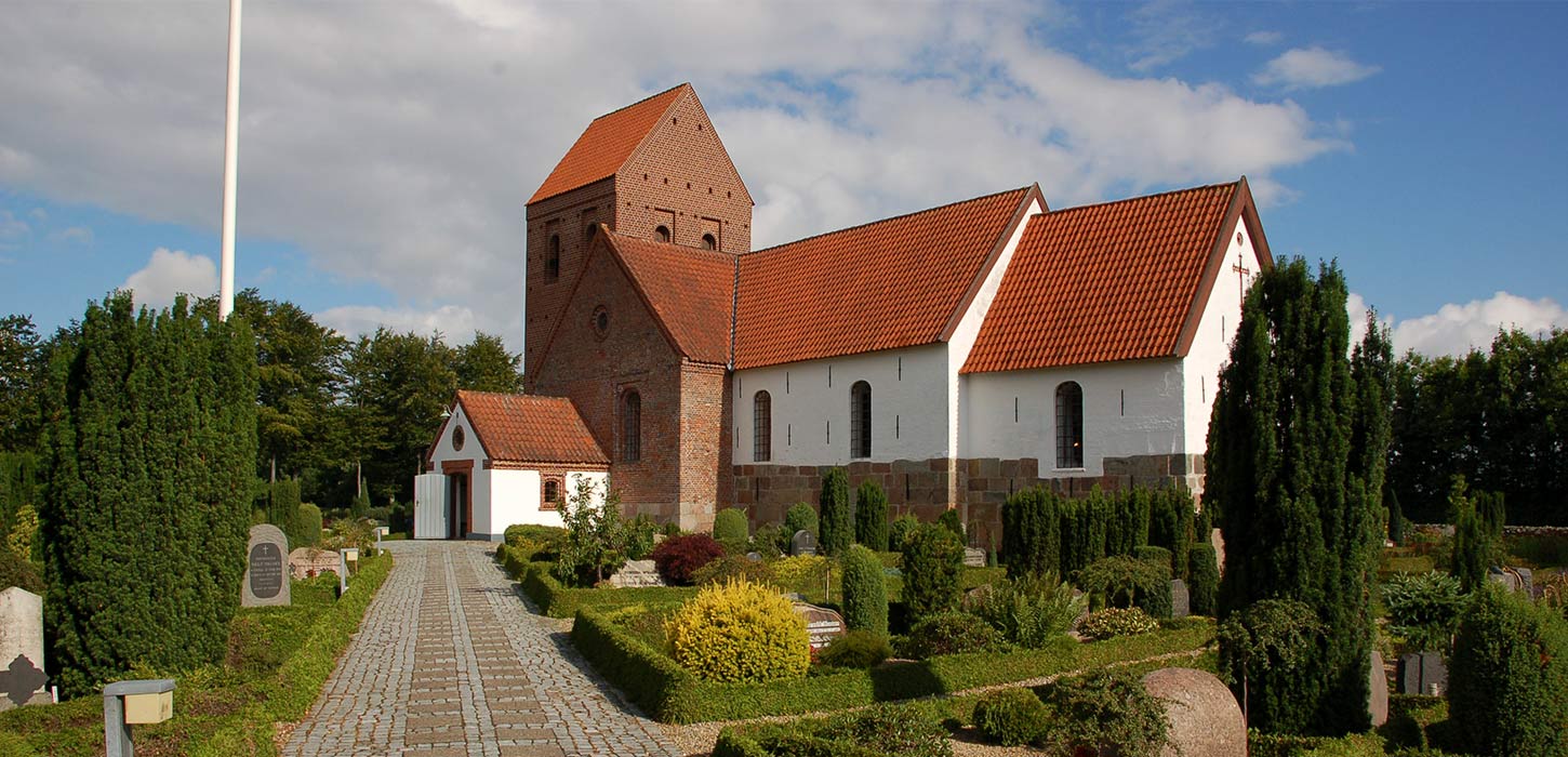 orbasse Kirke set udefra med hvidkalkede mure, rødt tegltag og omgivende kirkegård. Kirken er et stop på Kunstruten i Small Wonders – Heart of Jutland.