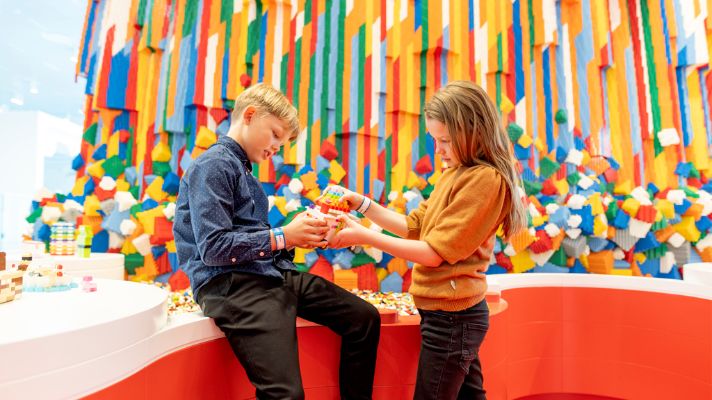Two children building lego in front of a colourful LEGO waterfall